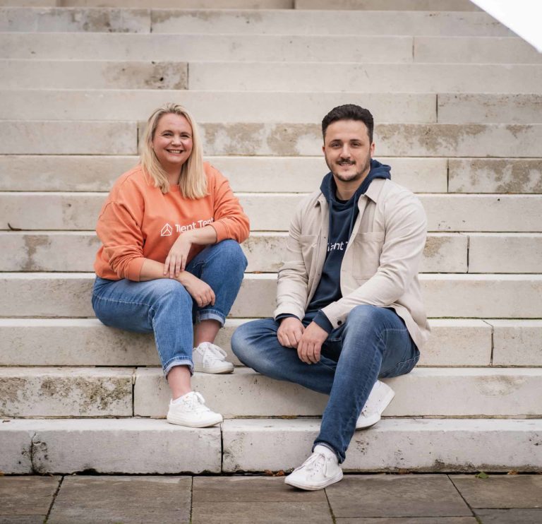 An image of a white woman and a white male, sitting on the steps of a building. These are the founders of Talent Tent.